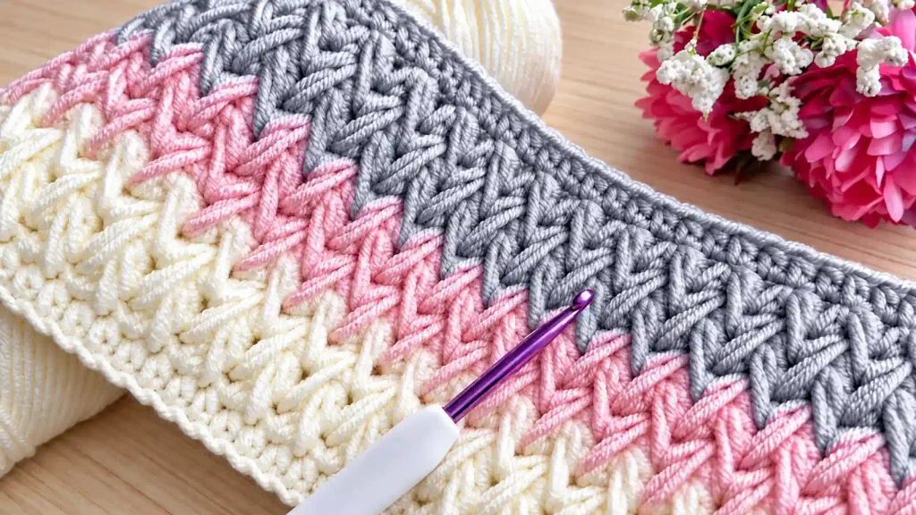 Muestra de punto en relieve a crochet en tonos rosa, gris y crema, con ganchillo morado.