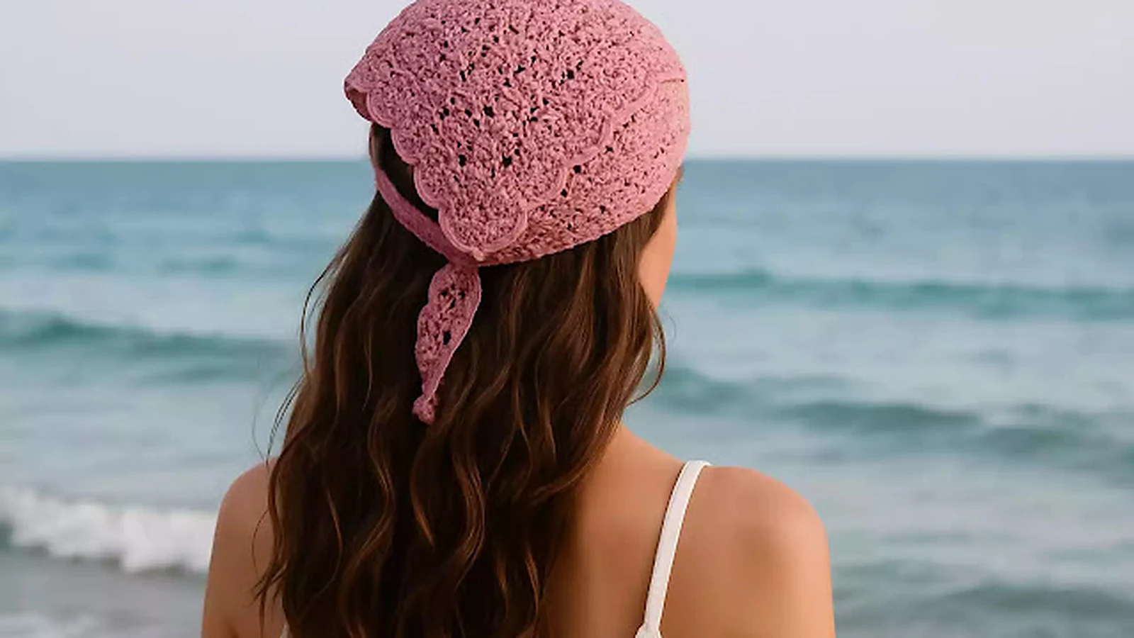 Bandana rosa tejida a crochet usada por una mujer frente al mar.
