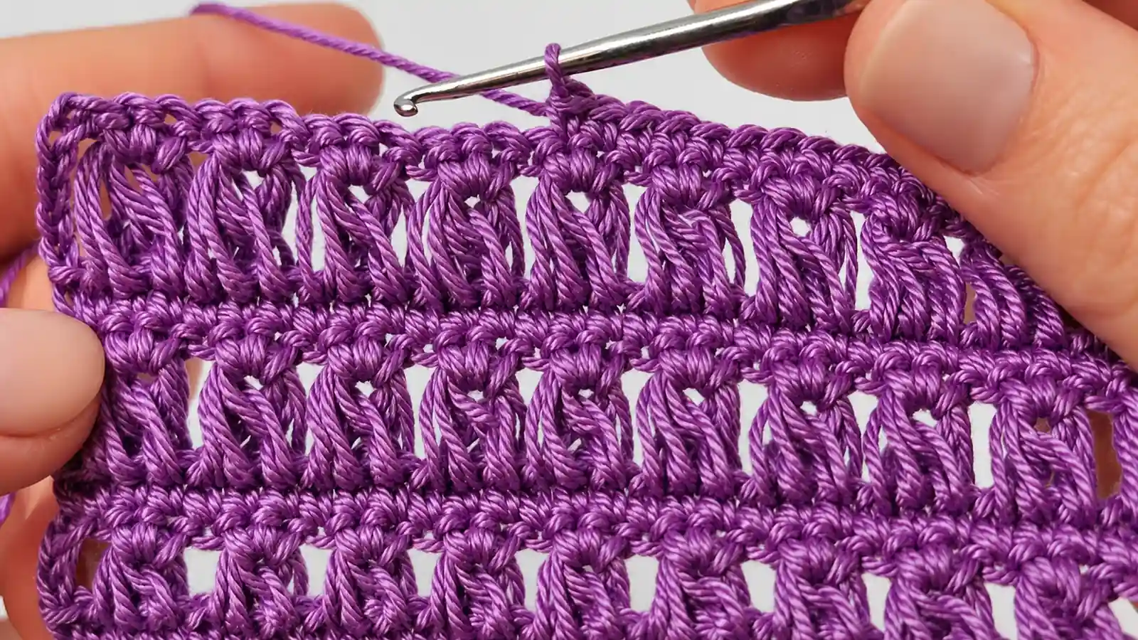Muestra de encaje a crochet en hilo morado, con lazadas alargadas y ganchillo metálico.